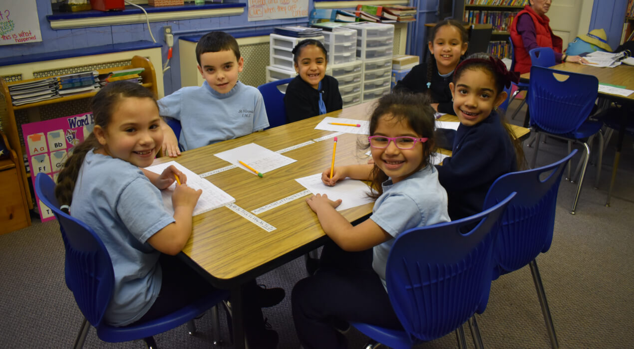 A group of small children sitting around a table at school 